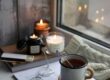 Rincón acogedor junto a la ventana con velas encendidas, un libro, gafas y una taza de té caliente, evocando privacidad e intimidad.