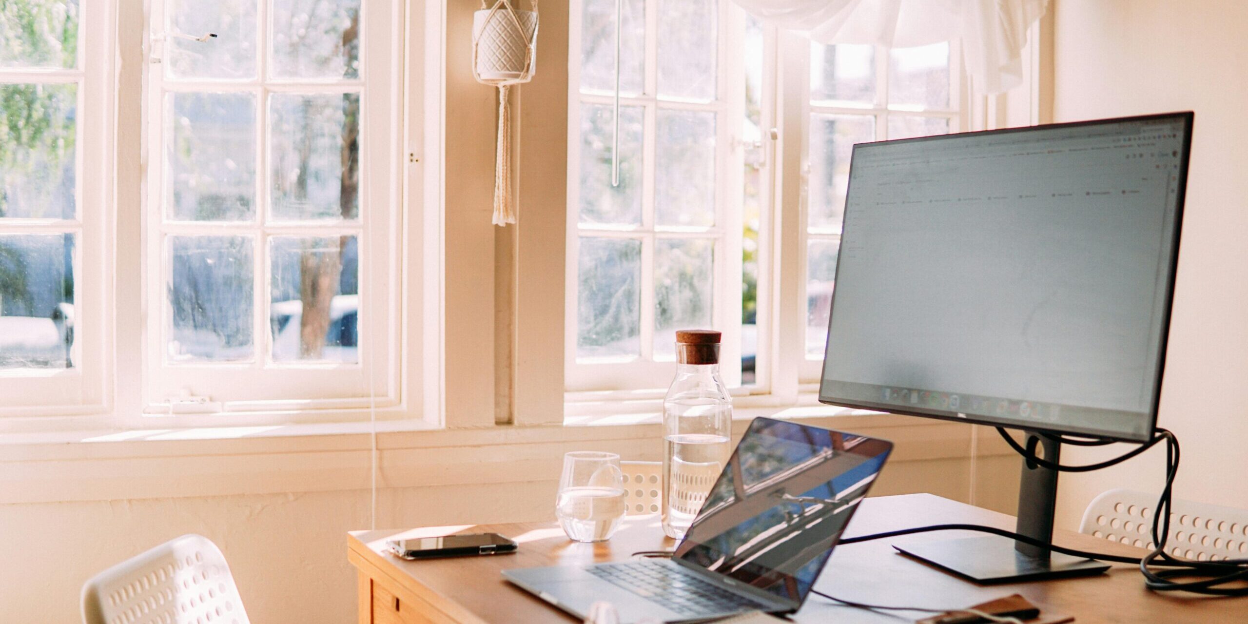 Espacio de trabajo minimalista con luz natural, un ordenador portátil y un monitor, ideal para la productividad y conexión.