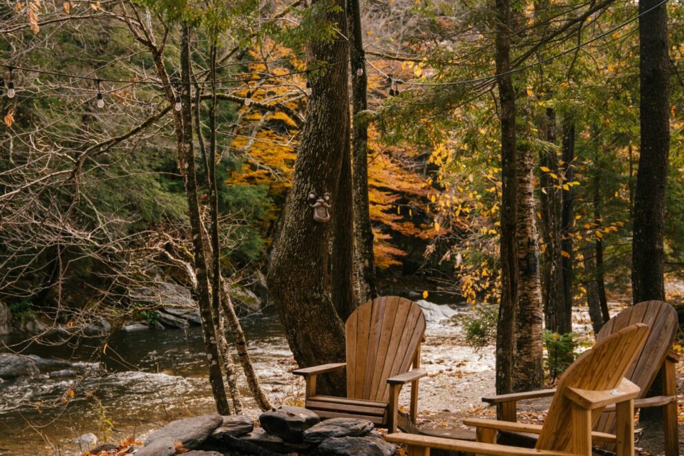 Sillas de madera junto a un río rodeado de árboles en otoño, evocando tranquilidad y conexión con la naturaleza.
